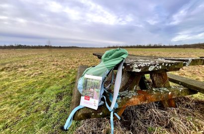 Rugzak en boekje Stellingenpad op een picknickbankje in een grasland omgeving met dreigende lucht