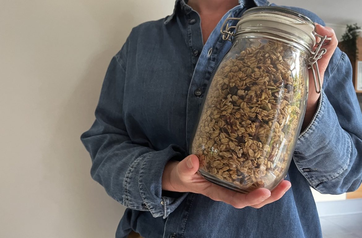 Pot zelfgemaakte granola wordt omhoog gehouden. Zelf granola maken: gezond, simpel en snel