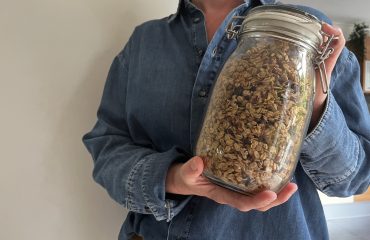 Pot zelfgemaakte granola wordt omhoog gehouden. Zelf granola maken: gezond, simpel en snel
