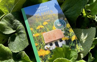 De dagen die komen, boek van Mélissa da Costa tegen een achtergrond van bladeren in een tuin