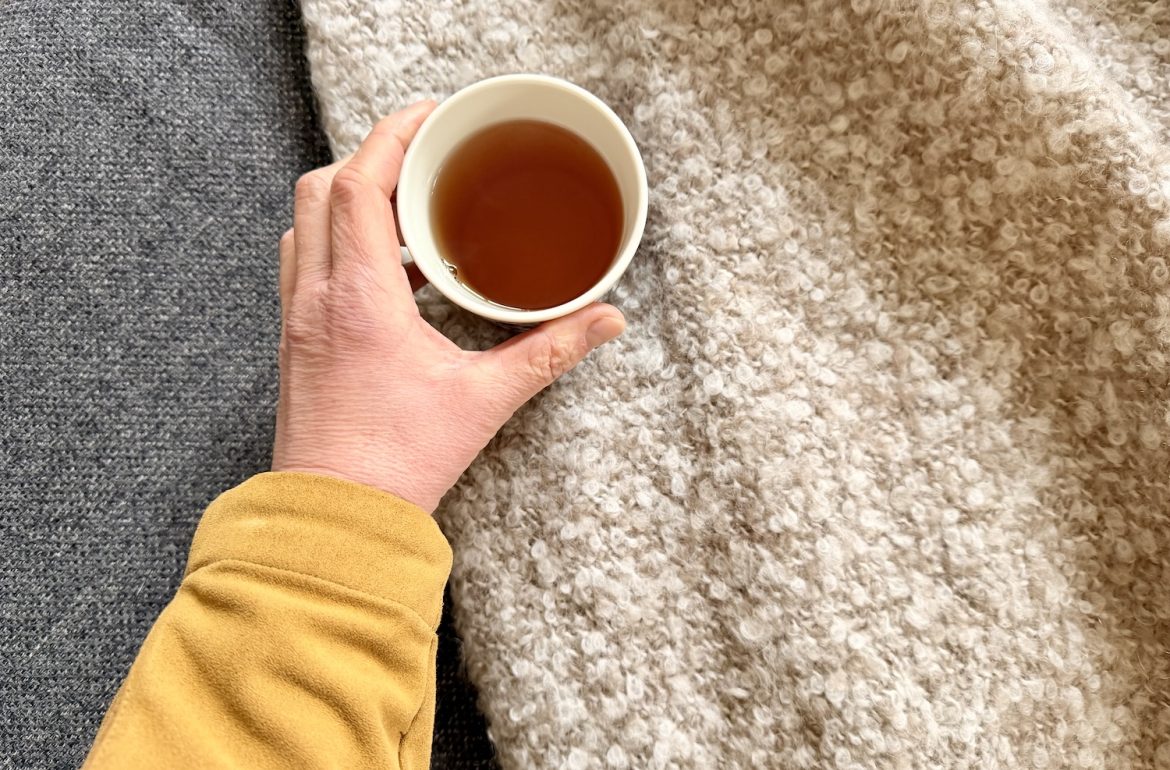 Hand met kop thee tegen een tweekleurige achtergrond. Bezinnende stemming en passend als hoofdfoto bij artikel over 50 worden en de overgang