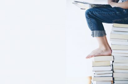 Boek op schoot en zittend op een stapel thrillers en andere boeken, leeslijst