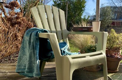 tuinstoel met op de leuning het boek Augustus van J.D. Barker naast een kop thee